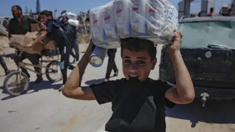 A child carries supplies on his head while walking from a GHF distribution centre in central Gaza.