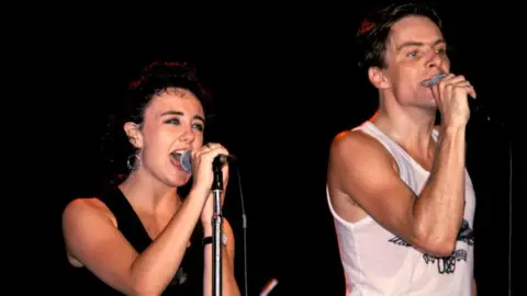 Getty Images Lorraine McIntosh and Ricky Ross singing on stage during the eighties. They are both wearing vest tops.