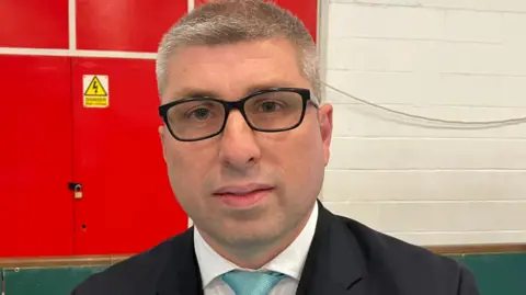 Mark Arnull, who is wearing a black suit and a light blue tie, looking directly at the camera. He is also wearing black framed glasses.