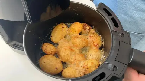 Potatoes are seen in an air fryer from the top down. The potatoes are yellow and have a yellow crust over the top of them.