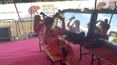 George King/BBC Two women drying their hair using hairdryers in front of a mirror.