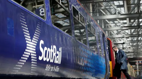 A ScotRail train Glasgow Central station. A passenger can be seen boarding one of the carriages. 