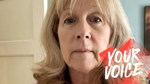 Tracy McGuire-Brown Tracy McGuire-Brown looks at the camera. She has cropped blonde hair and stands in a selfie position in front of an interior door and blue wall. The words Your Voice have been imposed on the bottom right of the picture