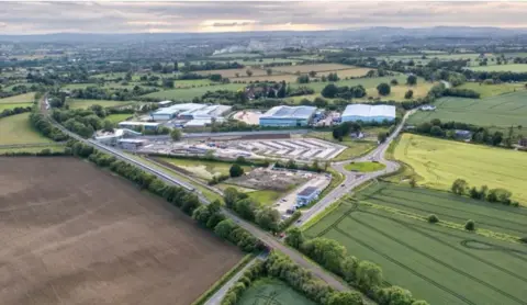 An aerial image mainly of fields, with trees and bushes. There are buildings in the middle of the photo.