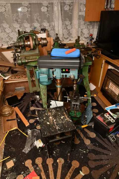 Metropolitan Police A drill press and metal lathe set up inside a caravan, surrounded by tools, wood offcuts and debris on the floor.