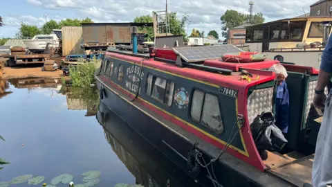 A narrowboat, on the water in a boatyard, being inspected