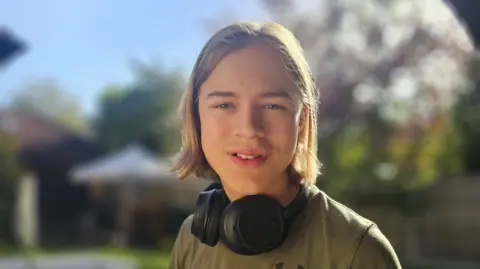 Harry's family A teenage boy with blond hair wearing a khaki t-shirt and large black headphones around his neck