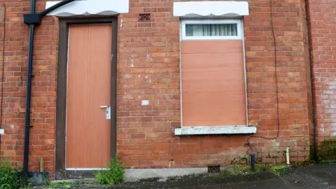 Pacemaker Red brick house in Belfast with door and windows boarded up after being attacked