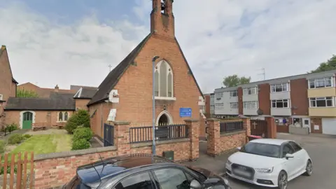 Google Streetview image of St Benedict's Church in Atherstone, Warwickshire, a red-brick church building in an urban street setting, with a brick wall and railings around it.