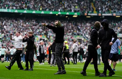 PA Media Several people stand on the pitch at a crowded football stadium, with more supporters in the stands behind them after fans spilled onto the field.