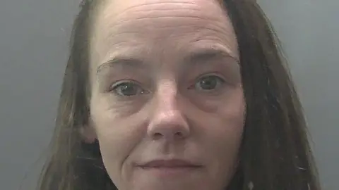 Cambridgeshire Constabulary Leah a woman, with shoulder length hair, smiling for her custody image.