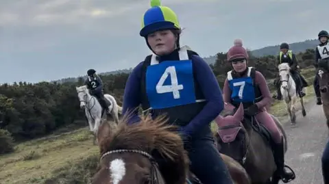 Maisy on a horse wearing a number four on her top and a blue and yellow helmet as she rises among others in the New Forest
