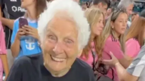 Elderly woman with white hair holds up sign asking Messi to marry her
