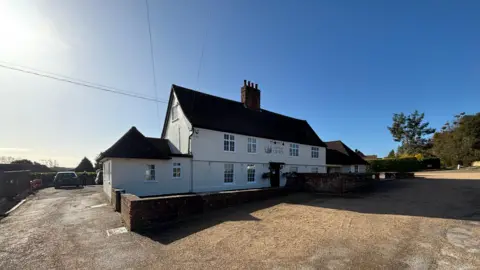 Luke Deal/BBC A general view of the exterior of the Ufford Crown pub on a sunny day. It is a white two-storey building with a large car park on its right and a smaller one behind it. 
