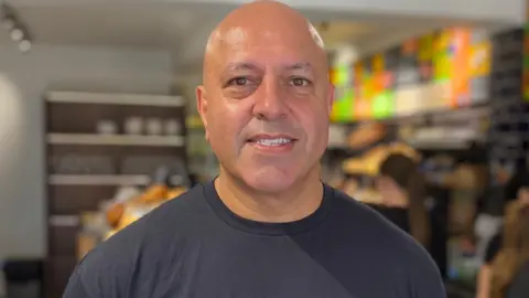 Michelin-starred chef Sat Bains inside a deli in West Bridgford, Nottinghamshire, wearing a dark t-shirt and looking at the camera.