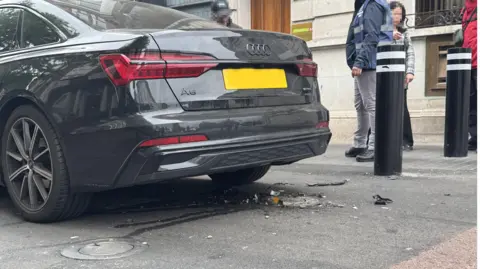 The back of a car hit by a rising bollard, with debris left on the road.
