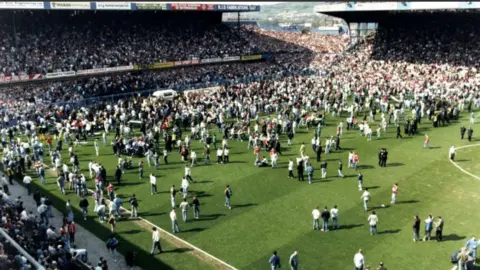 Fans on the pitch alongside a lone white ambulance near the goalmouth after the crush at the FA Cup semi-final between Liverpool and Nottingham Forest on 15 April 1989.