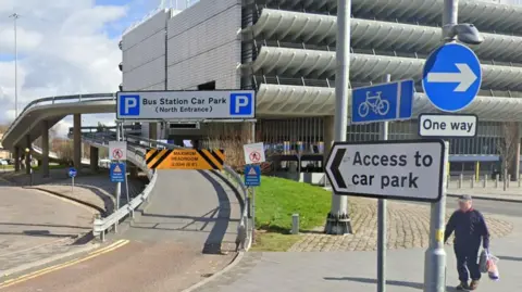 Road ramp entrance to Preston Bus Station with signs and pedestrian walking nearby.