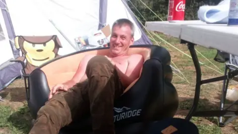 Family handout A shirtless Donald Excell grins at the camera as he lounges on an inflatable chair next to a tent on a summer's day in 2020.