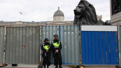 Reuters Two officers in front of a high metal barrier with one of the lions of Nelson's Column peering over the top.