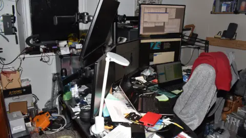 Metropolitan Police handout Orlin Roussev's office, with equipment strewn across and around a desk with a laptop and five monitors. 