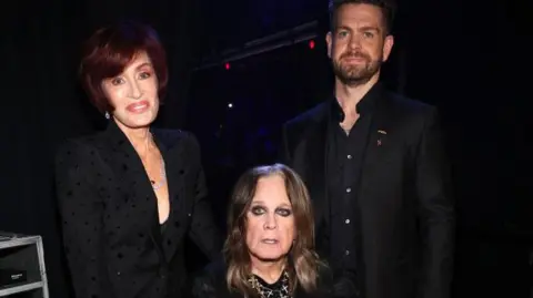 Getty Images Sharon, Ozzy and Jack, all in black looking towards a photographer. All three are smiling or have bemused expressions.