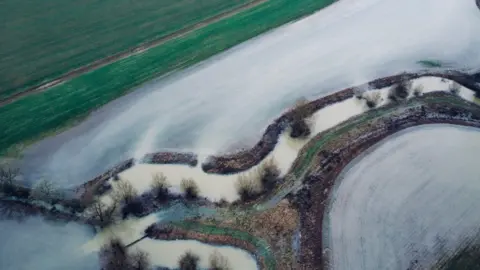 A brown river has burst its banks onto nearby fields.