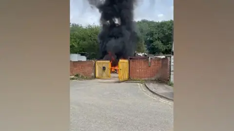 Fire behind yellow gates with smoke billowing up into the sky