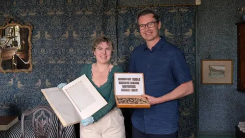Lucinda MacPherson Jason Sandy holds a box containing his donated Doves Type while standing next to curator Taryn Power who is holding open a large Doves Bible inside Emery Walker's House