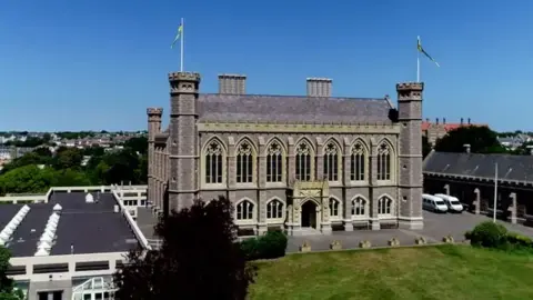 BBC An aerial view of Victoria College - an all boys school in Jersey which looks like a castle. Field in front and blue skies behind.