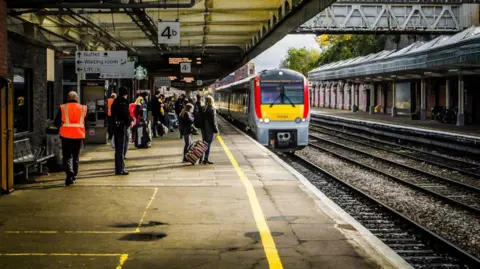 A train arrives at Shrewsbury Station, as passengers wait to board. There are signs above indicating they are standing on platform 4b.