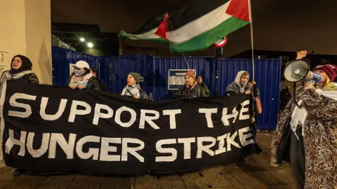 Getty Images Protesters hold up a sign reading 'Support the hunger strike' and wave Palestine flags