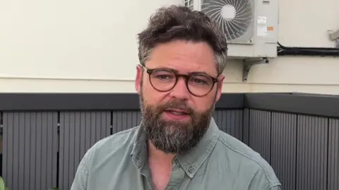 A man in a grey shirt. He has thick black curly hair. 