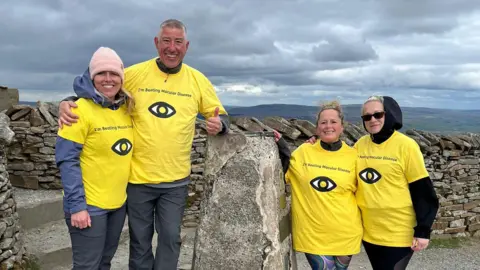 Contributed Mrs Blezard and some of the team stand at the top of a mountain. They all wear matching yellow T-shirts over the top of warmer clothes.