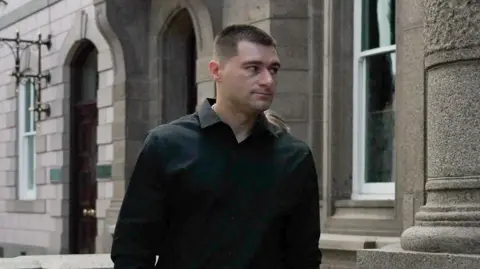 BBC A man wearing a black shirt walking into the royal court.