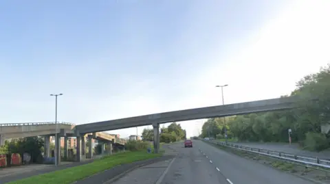 Google Footbridge over the road with car on it on a clear blue day.