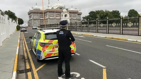 BBC/Phil Harrison A policeman stands by a car at the gated entrance to Gravesend Gurdwara