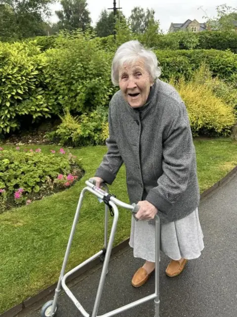 Supplied Hilda Jackson walking with a frame along a path in some gardens