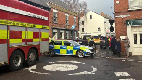 A fire engine and a police car in front of a cordon with people around it. 