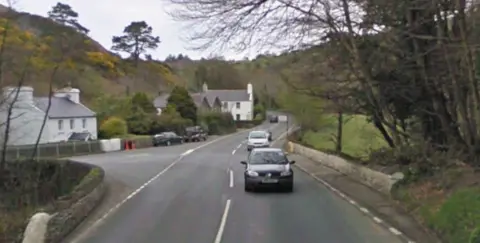 The Junction at Ballig Bridge. There are white houses on the left and trees on the right.