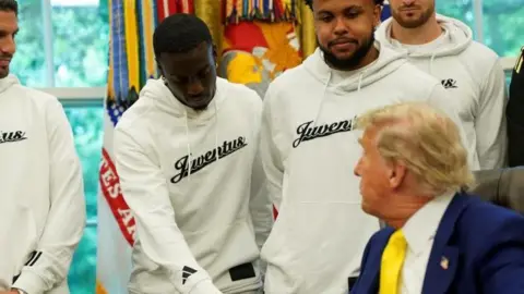 Reuters President Donald Trump wearing a suit and a yellow ties shakes hands with Timothy Weah, wearing white jumper 