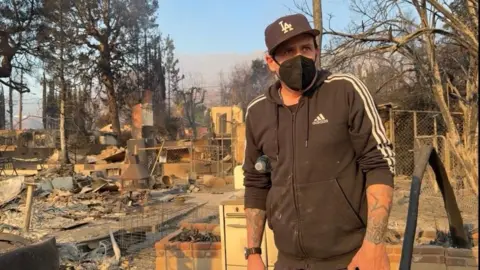 Daron wears a mask in a black Adidas hoodie while surveying the wreckage in his neighbourhood