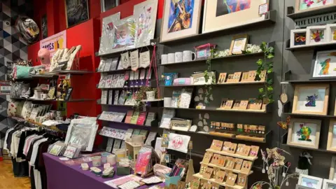 Dave Poulton A number of shelves and tables that are all displaying colourful products such as paintings, prints, homewares, T-shirts and mugs. 