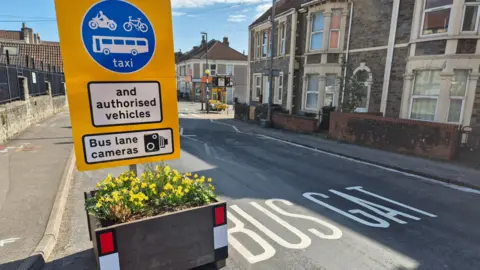 Sign of traffic sign near a bus gate with flower planters near homes.