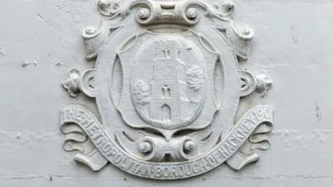 CAV Aerial A decorative crest carved into stone reading "The Metropolitan Borough of Hackney 1901"