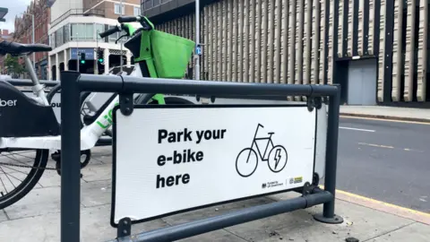 A e-bike and e-scooter parking rack in the city centre, with one e-bike parked inside.