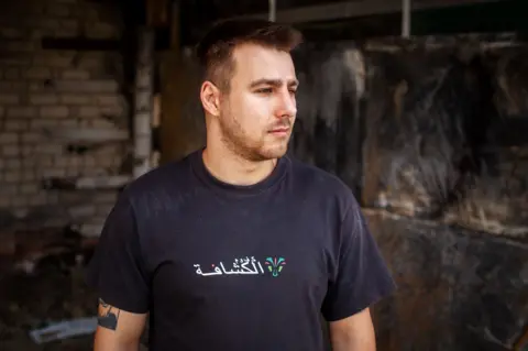 Stanislav Oysrous / BBC Dmytro Olifirenko wears a dark shirt, and the logo shows in a white and tattoo in an arm