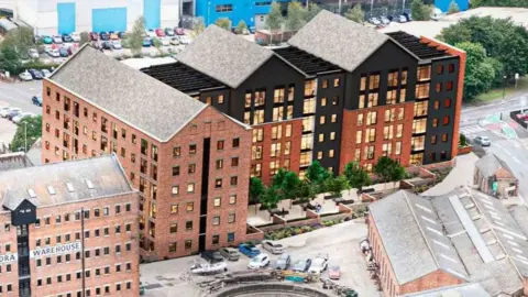 Canal and River Trust/Gloucester City Council A mocked-up design showing the outside of a six-storey block of flats. It i an industrial style, L-shaped building with red bricks and uniform windows. The right side of the building is half brick and half black paint. Some greenery, benches and cars are pictured at the base of the block, with a road and car park in the background.