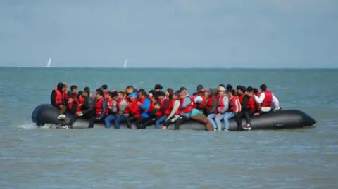 A large inflatable boat is packed with people wearing red life jackets. 