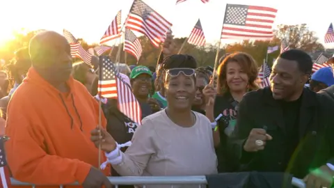 A woman holding an American flag between two men with the sun setting behind.